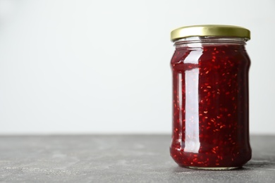 Photo of Jar of raspberry jam on grey table, closeup. Space for text