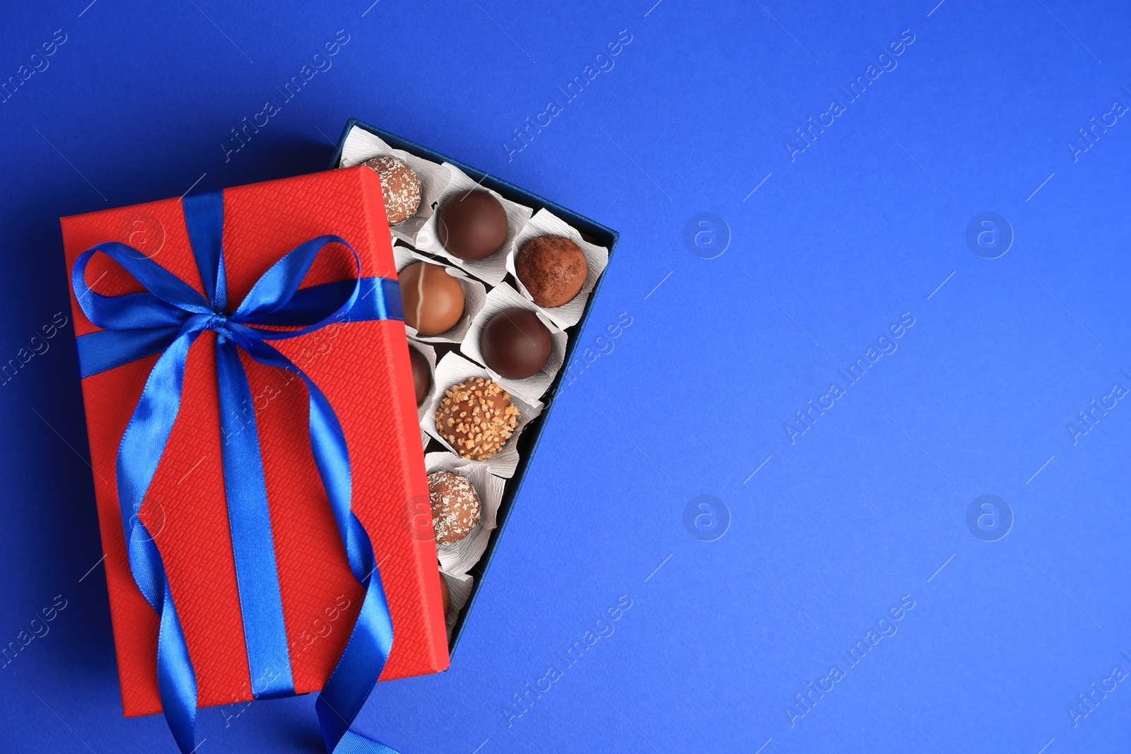 Photo of Box with delicious chocolate candies on blue background, top view. Space for text