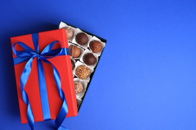 Photo of Box with delicious chocolate candies on blue background, top view. Space for text