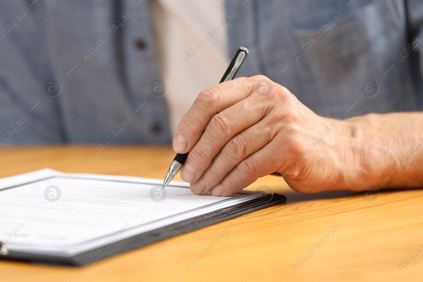 Photo of Senior man signing Last Will and Testament at wooden table, closeup