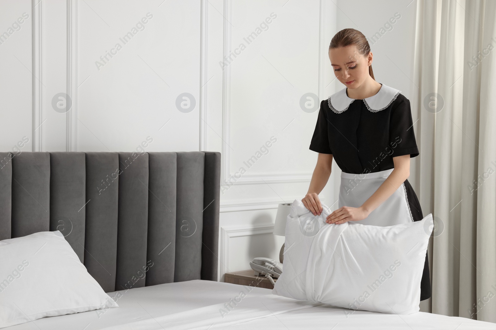 Photo of Young maid making bed in hotel room. Space for text