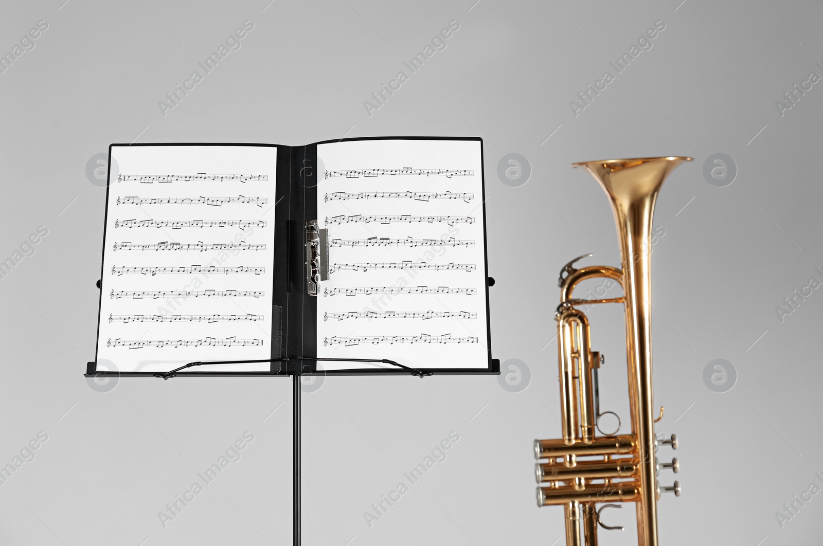 Photo of Trumpet and note stand with music sheets on grey background