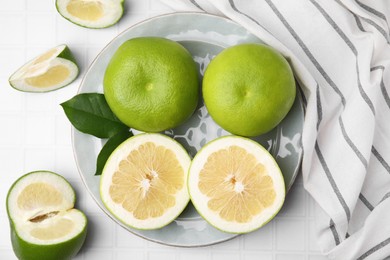 Photo of Whole and cut sweetie fruits with green leaves on white tiled table, flat lay