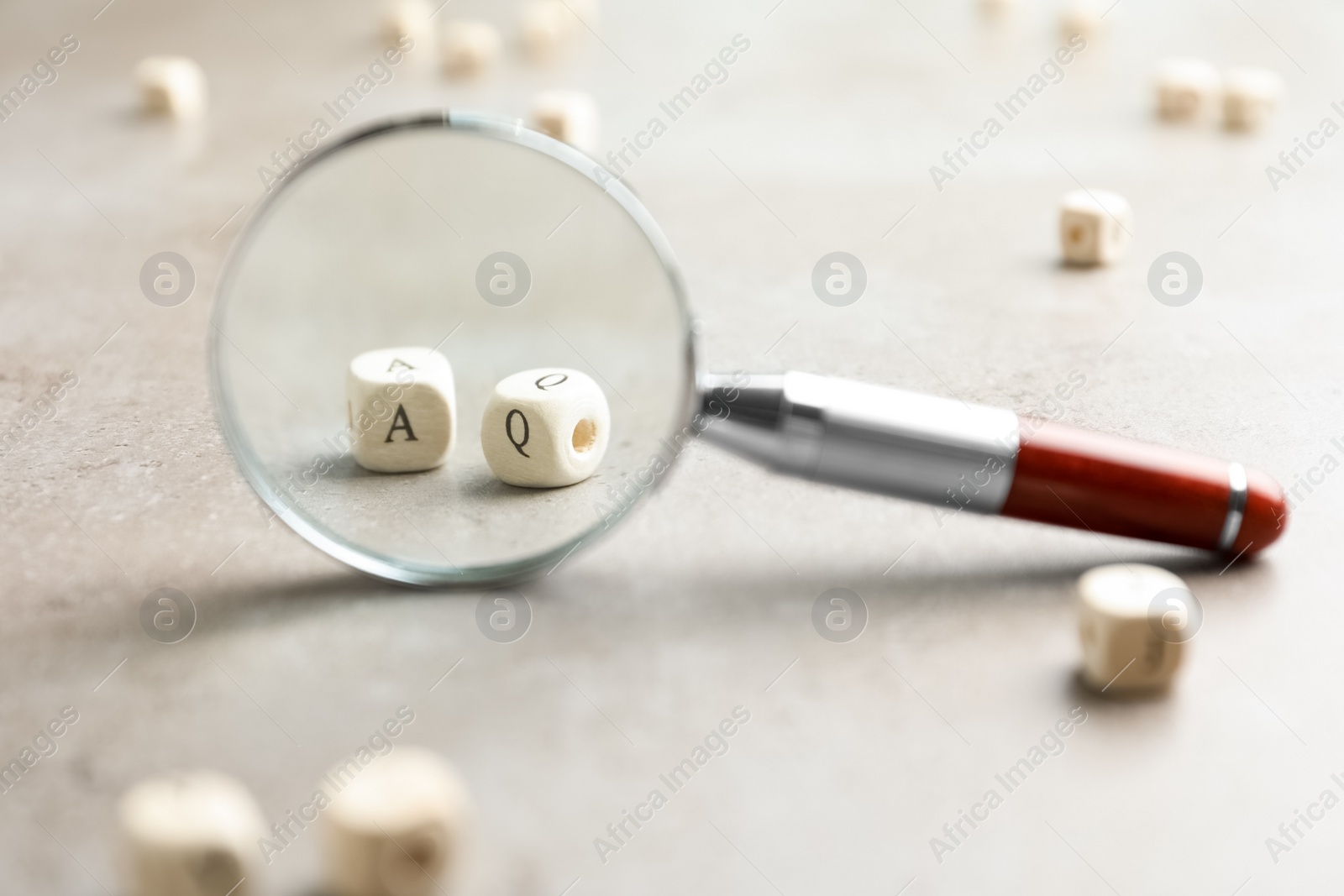 Photo of View on cubes with letters A and Q through magnifying glass at light grey stone background, closeup. Find keywords concept