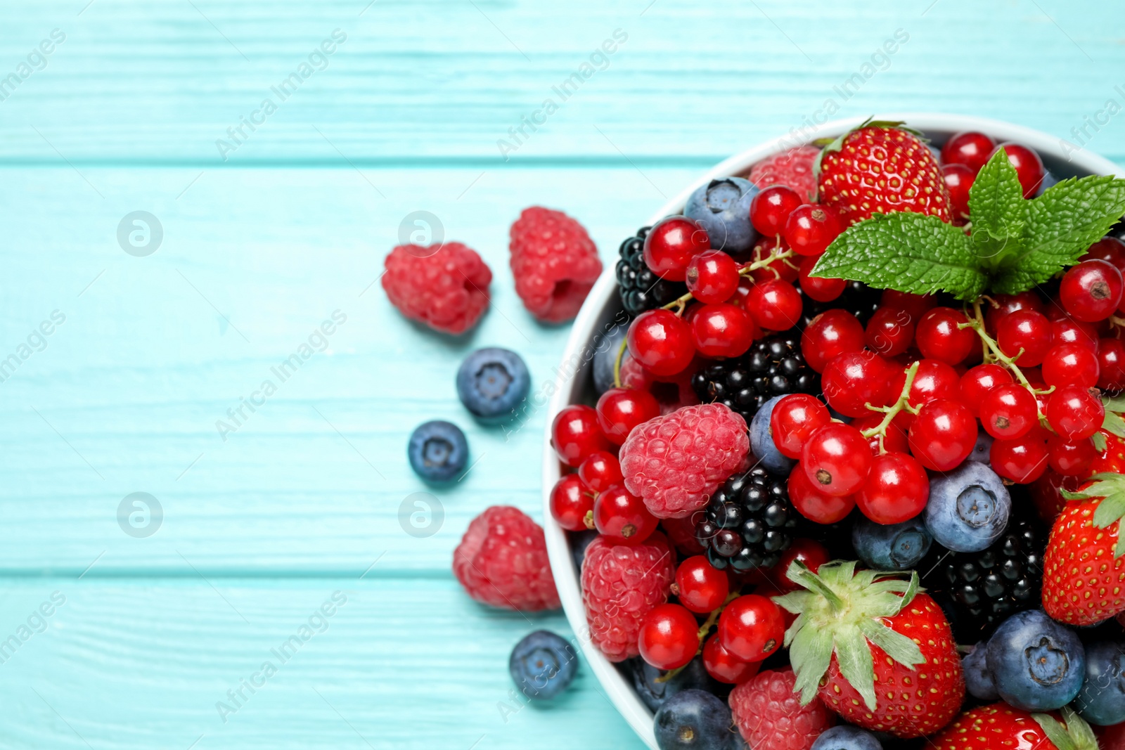 Photo of Mix of different fresh berries and mint in bowl on light blue wooden table, flat lay. Space for text