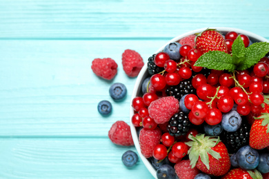 Photo of Mix of different fresh berries and mint in bowl on light blue wooden table, flat lay. Space for text