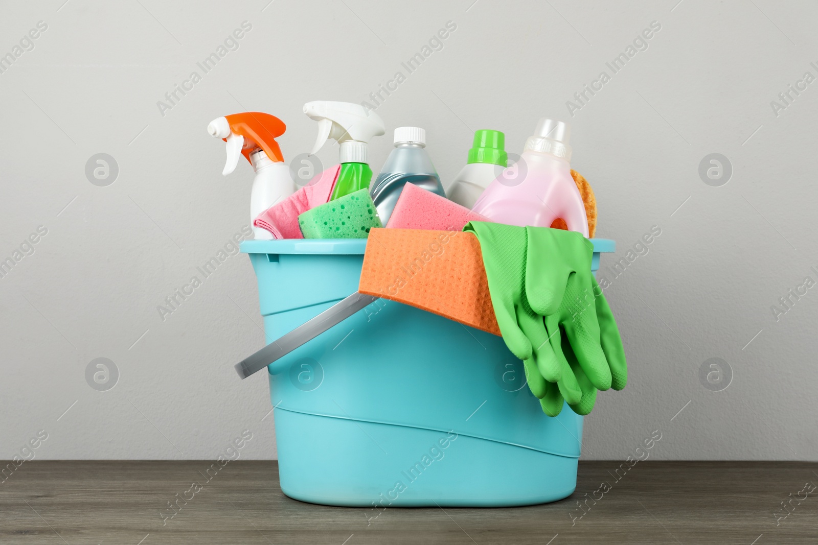 Photo of Light blue bucket with cleaning products on wooden table