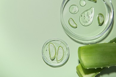 Photo of Cut aloe vera and drops of cosmetic gel on light green background, flat lay. Space for text