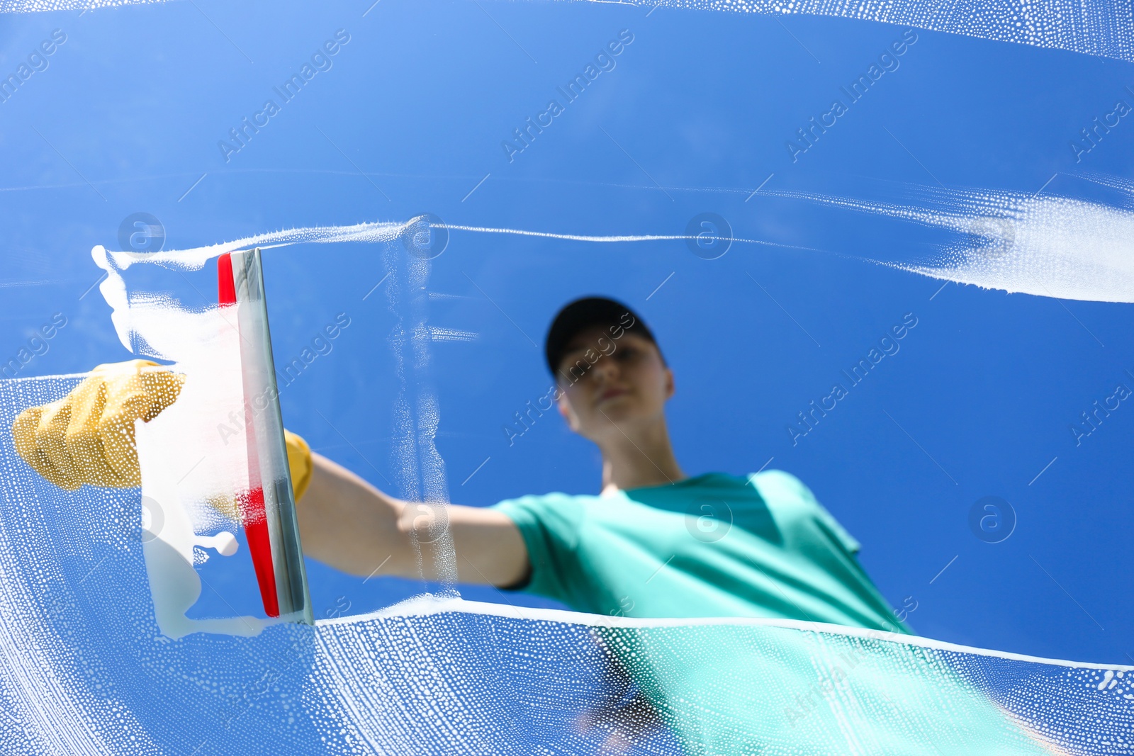 Photo of Woman cleaning glass with squeegee on sunny day