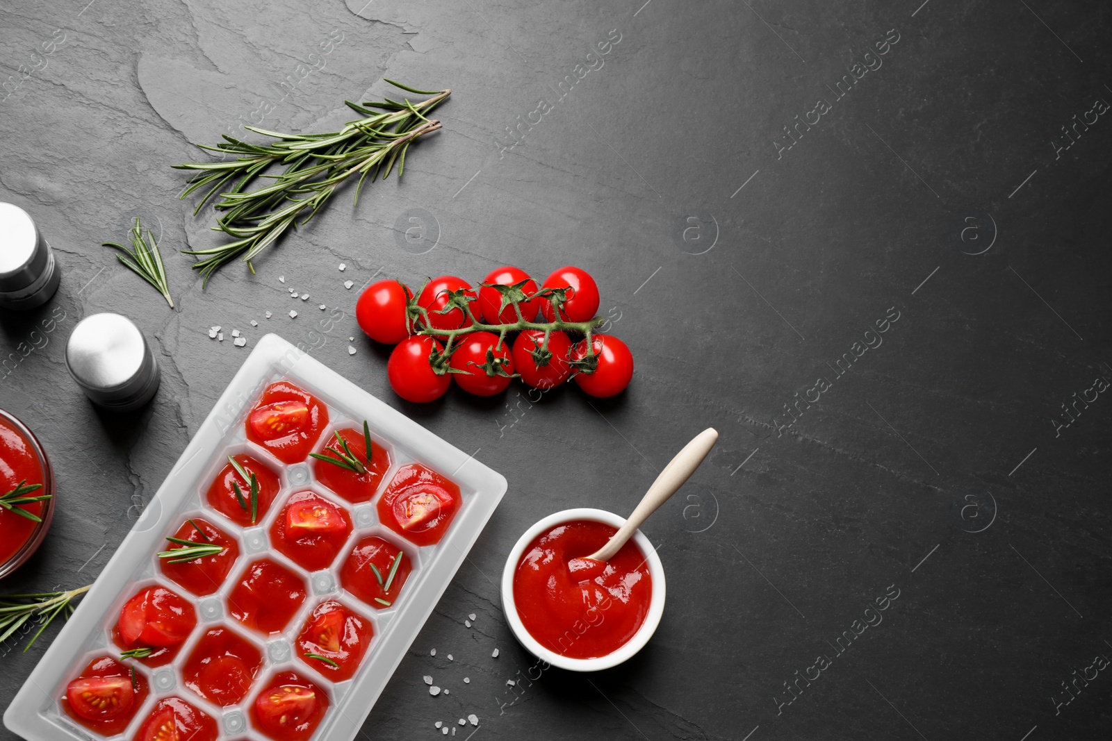 Photo of Ice cube tray with tomatoes, sauce and fresh rosemary on grey table, flat lay