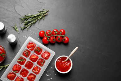 Photo of Ice cube tray with tomatoes, sauce and fresh rosemary on grey table, flat lay