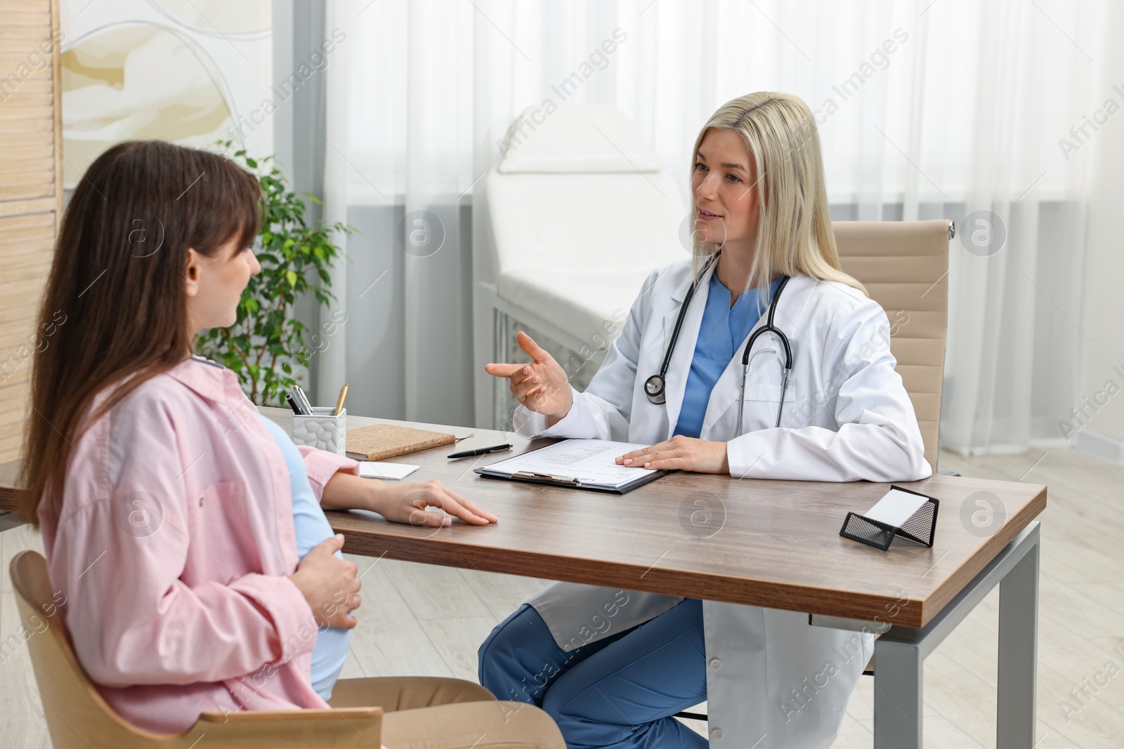 Photo of Smiling doctor consulting pregnant patient at table in clinic