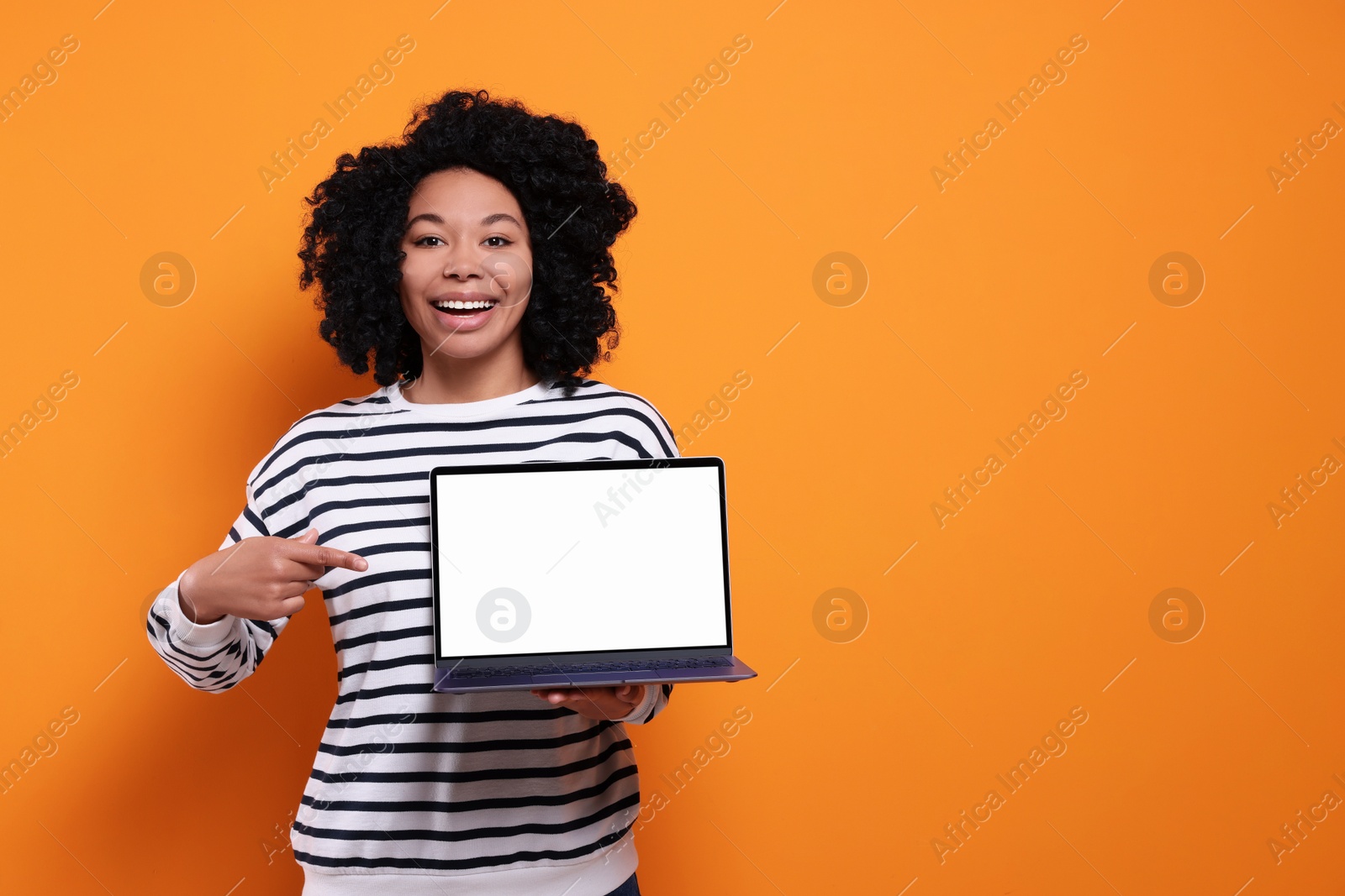 Photo of Happy young woman showing laptop on orange background. Space for text