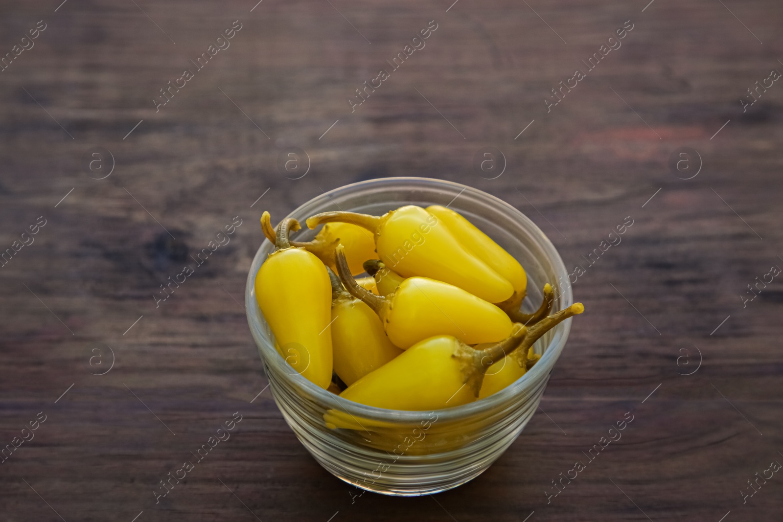 Photo of Bowl of pickled yellow jalapeno peppers on wooden table