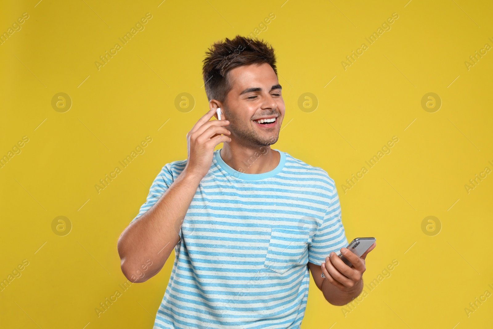 Photo of Happy young man with smartphone listening to music through wireless earphones on yellow background