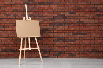 Wooden easel with blank board near brick wall indoors. Space for text