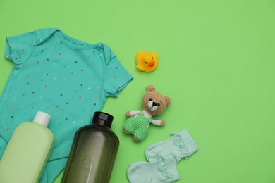 Photo of Bottles of laundry detergents, baby clothes and toys on light green background, flat lay. Space for text