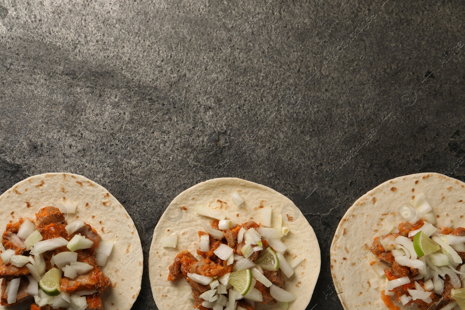 Photo of Delicious tacos with vegetables, meat and lime on grey textured table, flat lay. Space for text