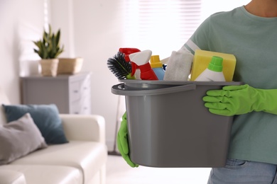 Photo of Woman holding bucket with cleaning supplies in living room, closeup. Space for text