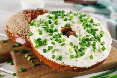 Photo of Delicious bagel with cream cheese and green onion on wooden board, closeup