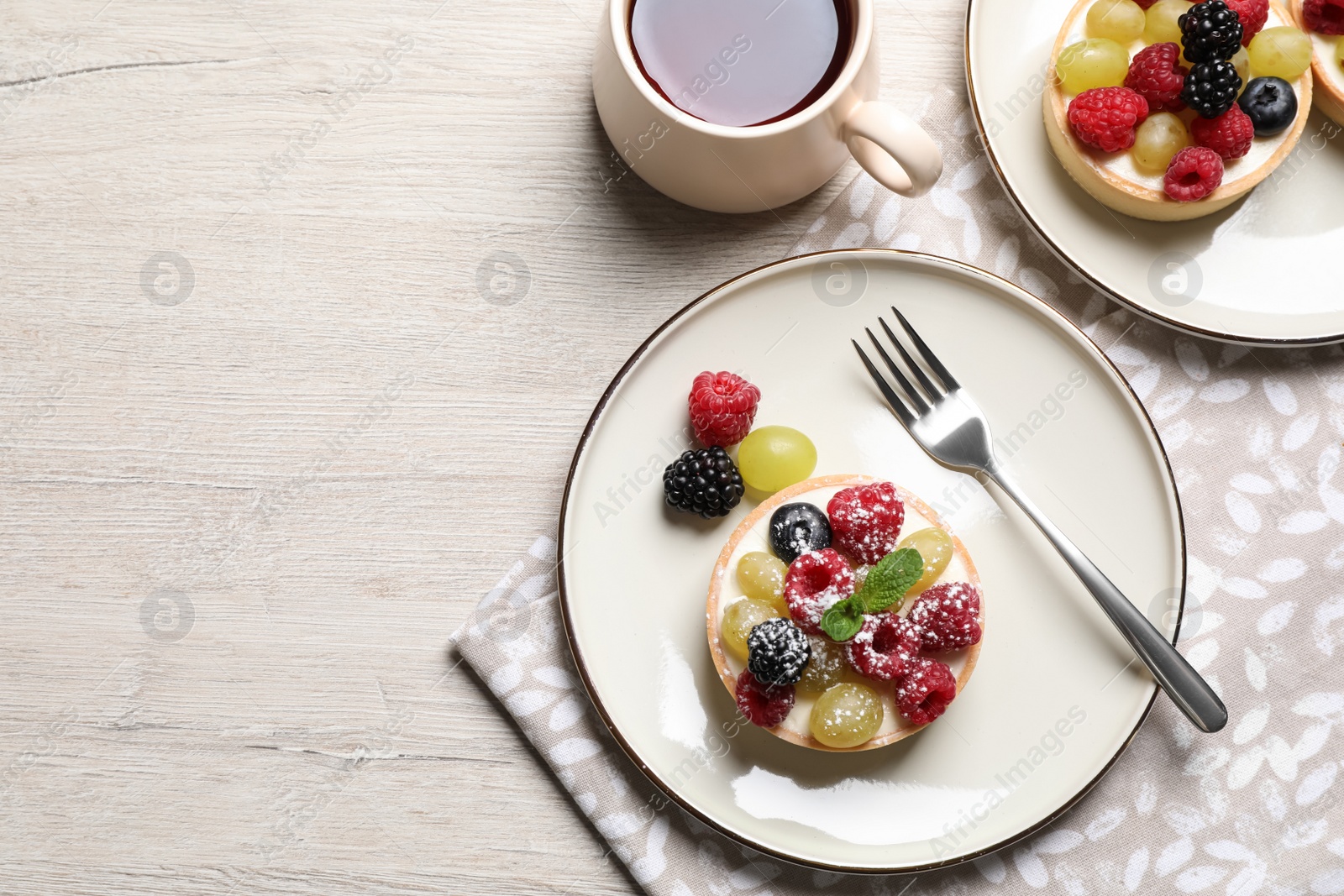 Photo of Delicious tartlets with berries and tea on light wooden table, flat lay. Space for text