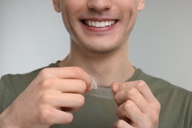 Young man with whitening strips on light grey background, closeup