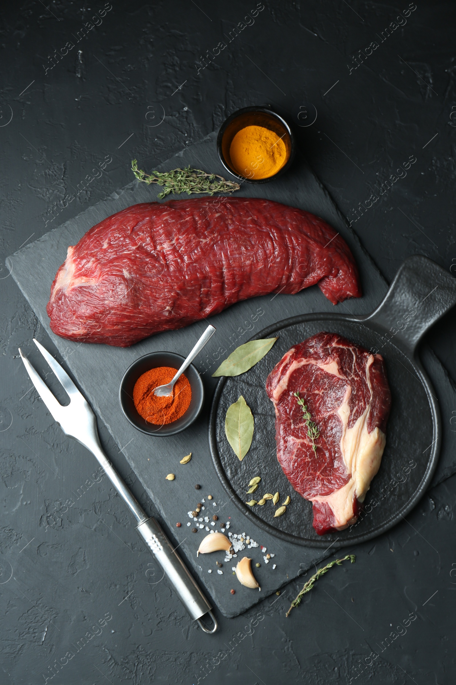 Photo of Pieces of raw beef meat and spices on black table, flat lay