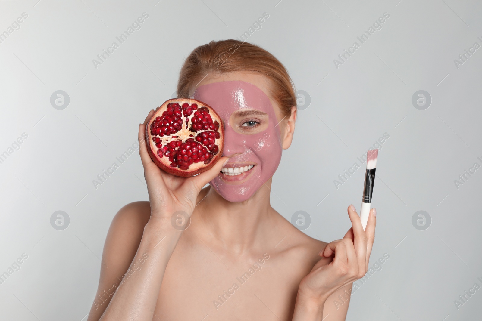 Photo of Young woman with pomegranate face mask and fresh fruit on light grey background