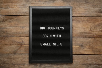 Photo of Black letter board with motivational quote Big Journey Begin with Small Steps on wooden background, top view