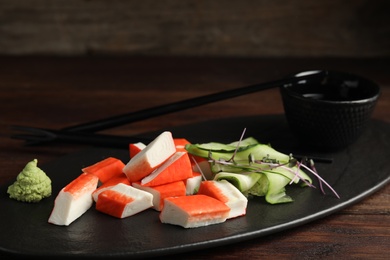 Photo of Fresh crab sticks with cucumber served on dark table, closeup