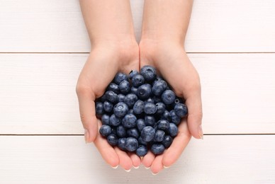 Photo of Woman with heap of tasty blueberries on white wooden background, top view
