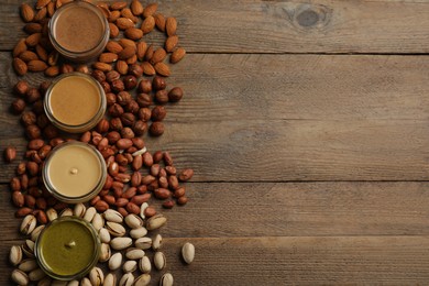 Photo of Jars with butters made of different nuts and ingredients on wooden table, flat lay. Space for text