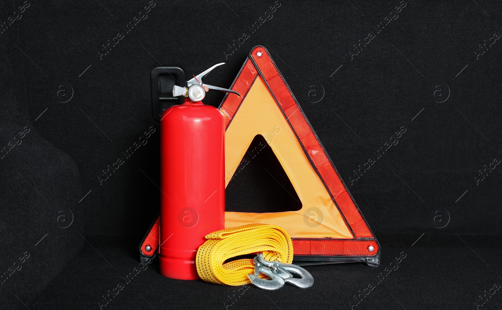 Photo of Red fire extinguisher, towing strap and foldable emergency warning triangle in trunk. Car safety