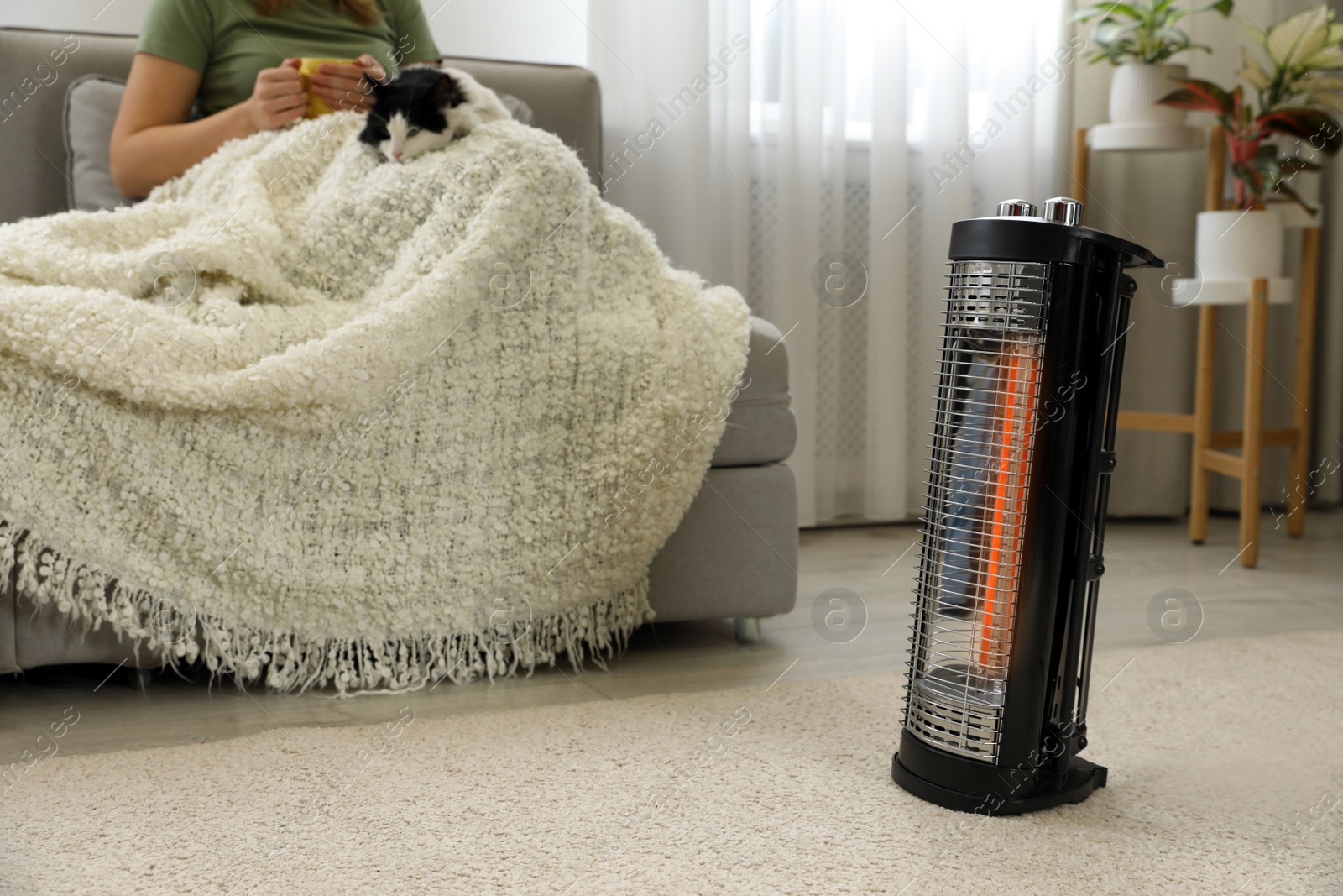 Photo of Woman with cat at home, focus on electric halogen heater, closeup