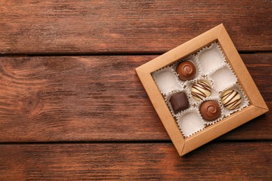 Photo of Partially empty box of chocolate candies on wooden table, top view. Space for text
