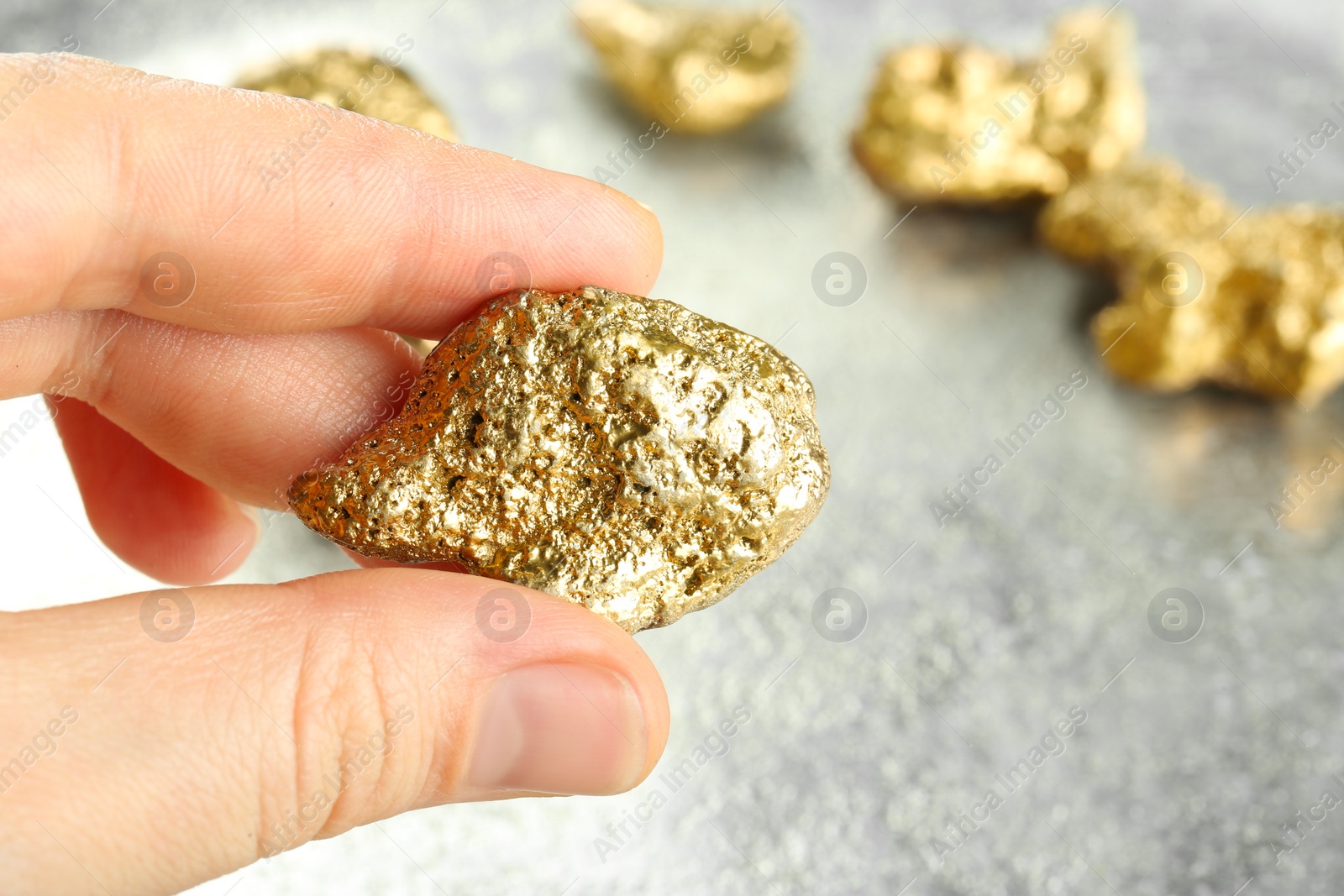 Photo of Woman holding gold nugget at light grey table, closeup. Space for text