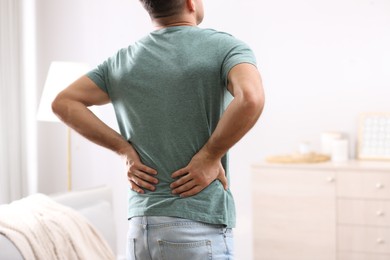 Photo of Man suffering from back pain at home. Bad posture problem