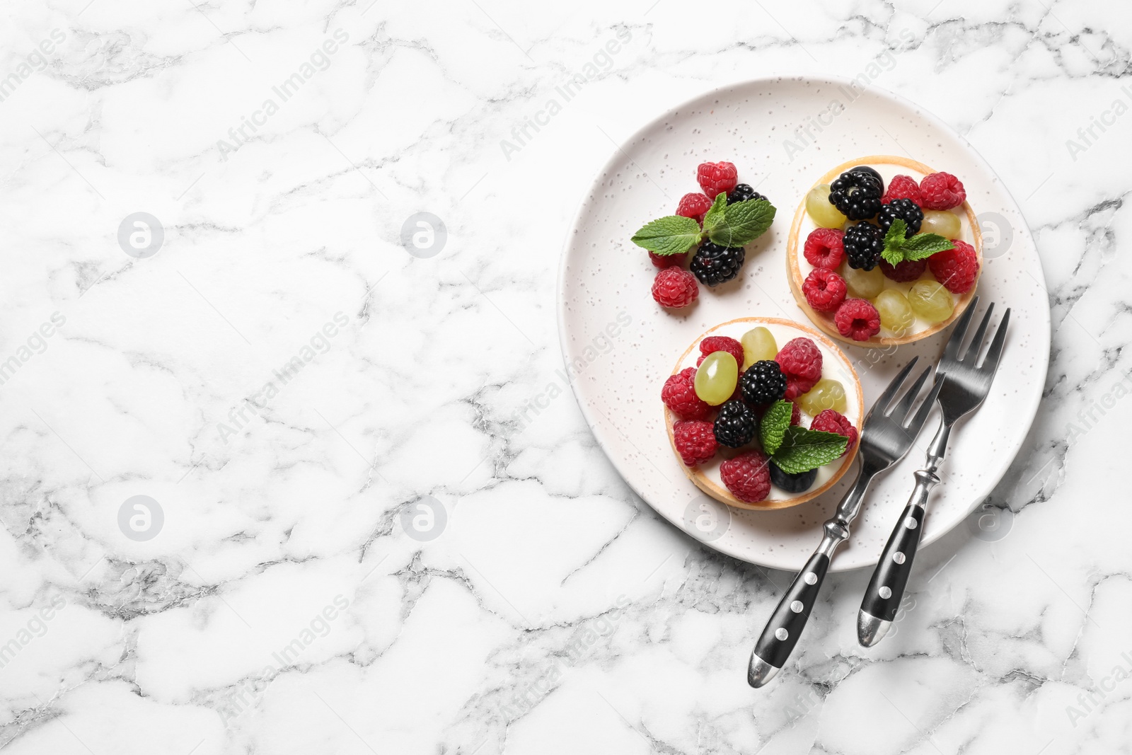 Photo of Delicious tartlets with berries on white marble table, top view. Space for text
