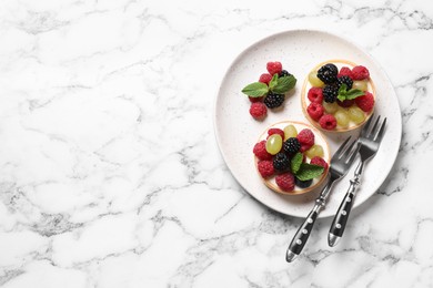 Delicious tartlets with berries on white marble table, top view. Space for text