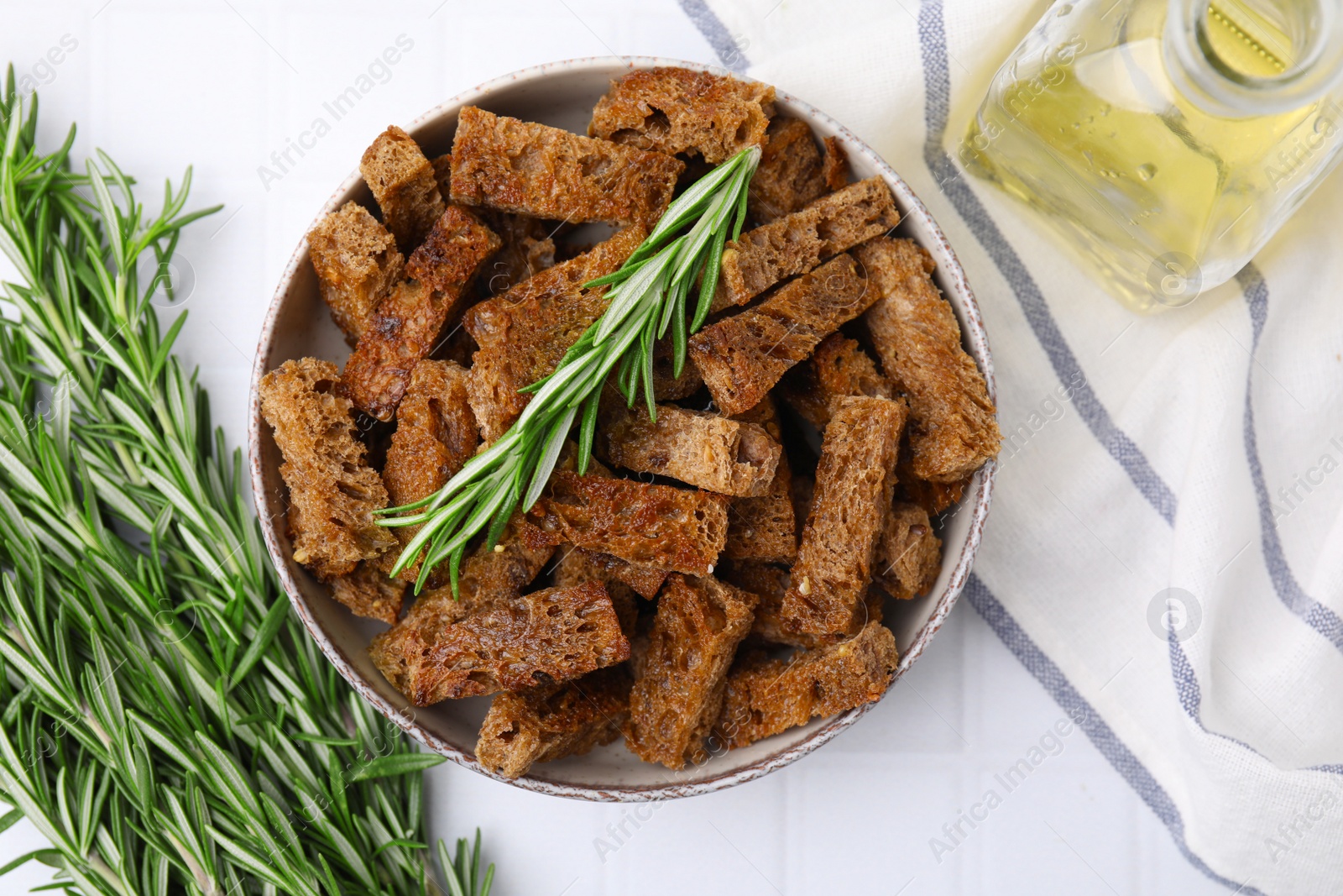 Photo of Crispy rusks with rosemary on white tiled table, flat lay