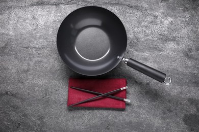 Empty iron wok and chopsticks on grey table, flat lay