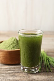 Photo of Wheat grass drink in shot glass on wooden table, closeup