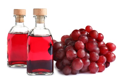 Photo of Bottles with wine vinegar and fresh grapes on white background