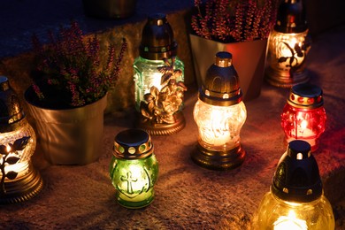 Photo of Different grave lanterns with burning candles on stone surface at night