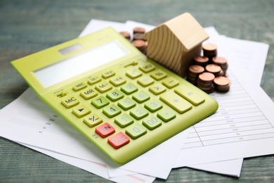 House model with coins, documents and calculator on wooden table, closeup. Real estate agent service