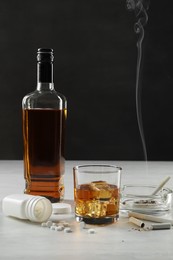 Alcohol and drug addiction. Whiskey in glass, bottle, cigarettes and pills on white table