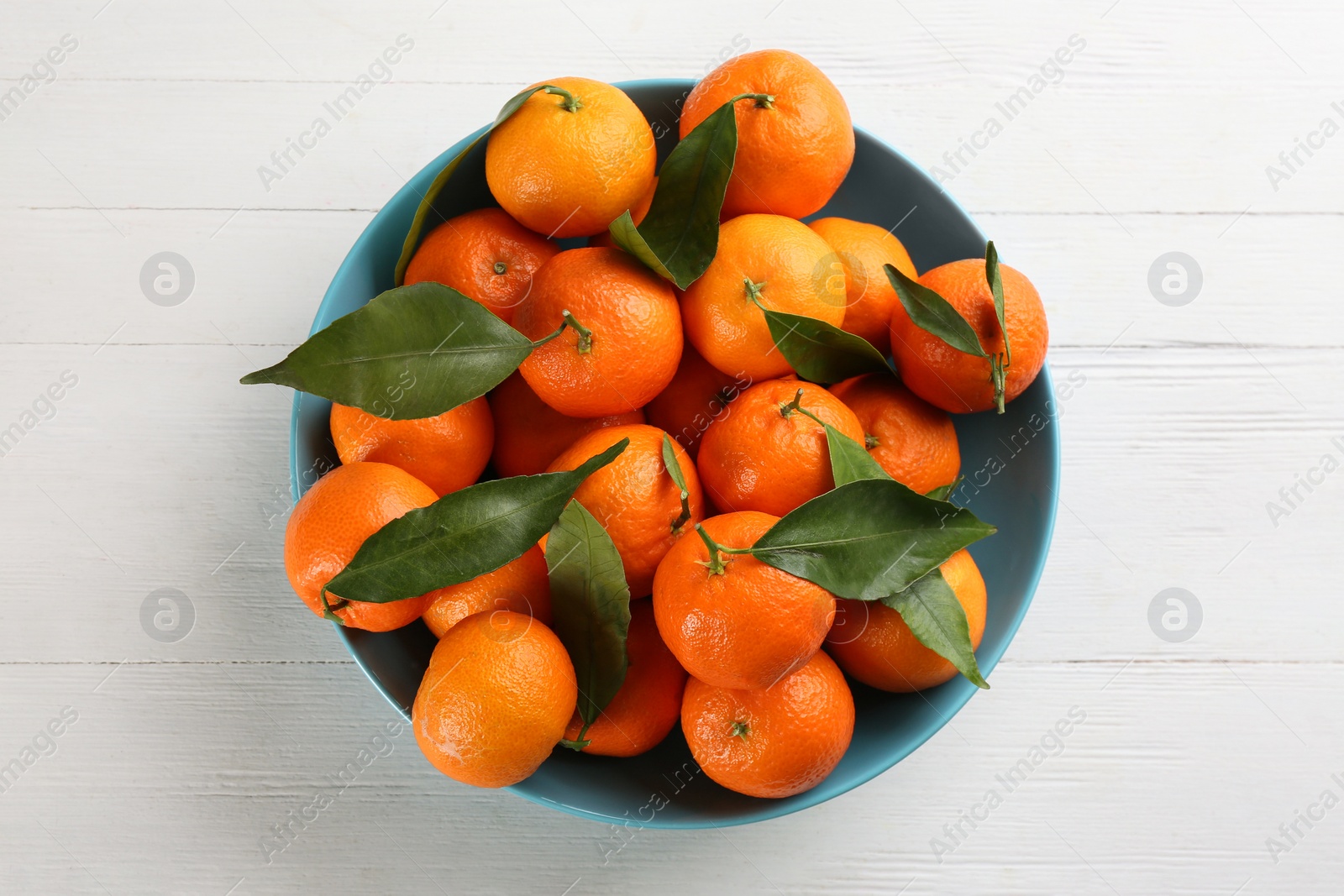 Photo of Fresh ripe tangerines with green leaves on white wooden table, top view