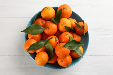 Fresh ripe tangerines with green leaves on white wooden table, top view