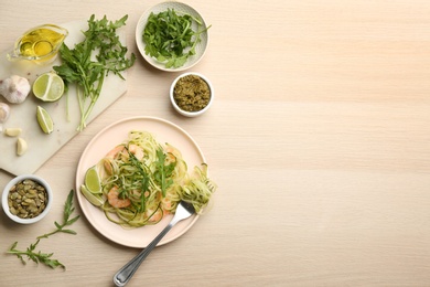 Photo of Tasty zucchini pasta with shrimps and arugula served on wooden table, flat lay. Space for text