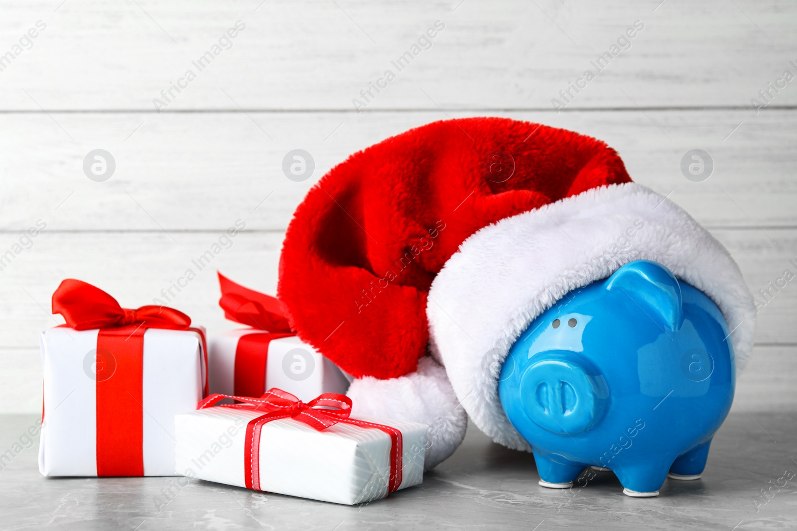 Photo of Piggy bank with Santa hat and gift boxes on grey table